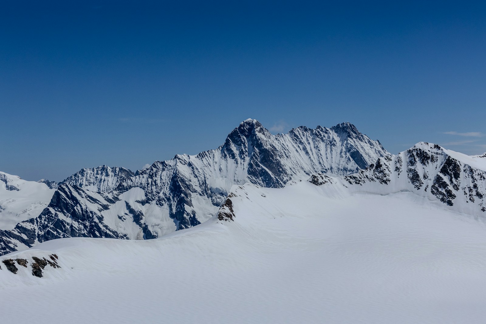 A mountain range covered in snow under a blue sky