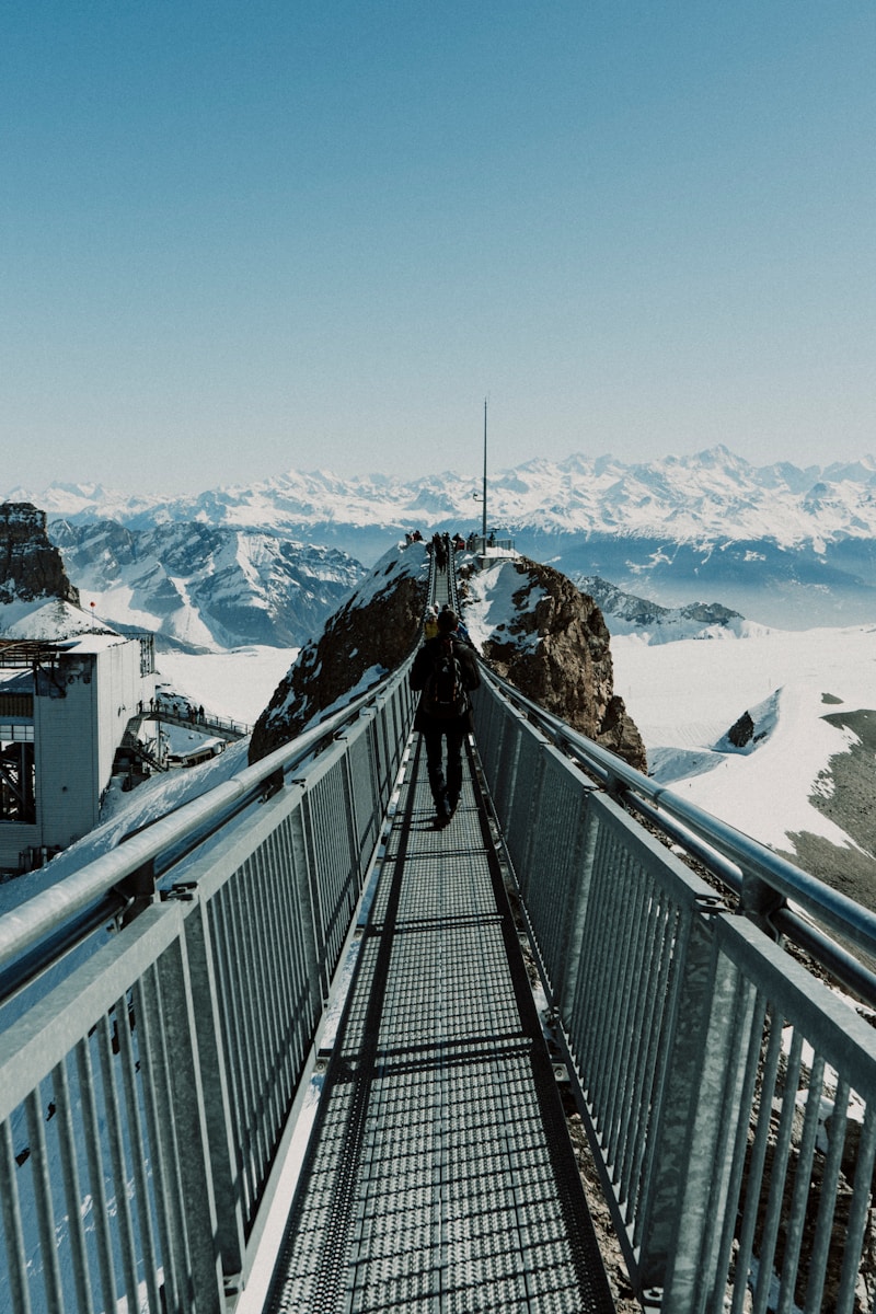 a man walking across a bridge over a snow covered mountain